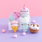 Group shot of five of the Pusheen Ice Cream characters sitting on white pedestals on a purple surface in front of a pink background. The Ice Cream characters included in this shot are Ice Pop Pusheen, Ice Cream Cup Pusheen, Strawberry Ice Cream Pusheen, Milkshake Pusheen, and Ice Cream Cake Pusheen. 