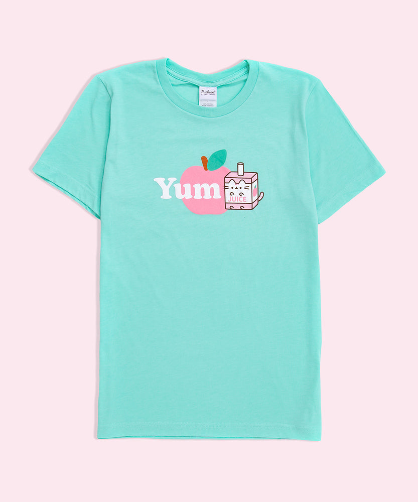 A mint green graphic tee against a light pink background. The graphic features Pusheen as Juice Box Sips next to the word ‘Yum’ in white, both in front of a pink apple. 
