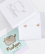 Gold Vermeil finish of Pusheen Lazy Stud Earrings in their white packaging box. The earrings are accompanied by the lid of the packaging box and a mint green informational card about the earrings.