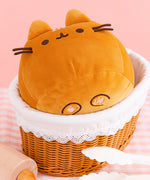 This view shows the hidden toe beans on the plush. The black embroidered paws have light pink ovals that mimic a cat’s paw pad. The squisheen sits inside a brown and white breadbasket. 