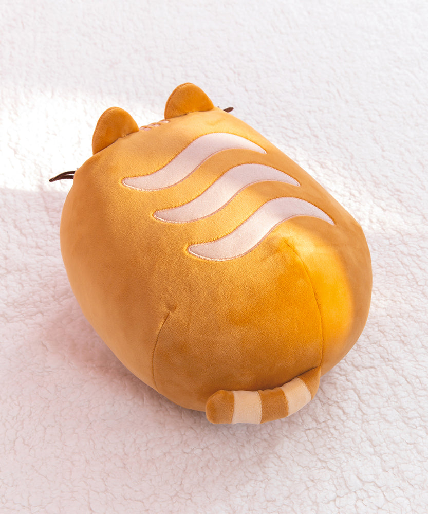 Back view of the loaf squisheen. The oval shaped plush has light cream wavy stripes on the top of the plush. At the back bottom of the plush is a light brown and cream striped tail. 