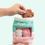 Hand holds the brown Pusheen Meowshmallow out of the plush bag containing white and pink Meowshmallows. Another hand holds the Pusheen Meowshmallows bag has a white seal, mint green top portion, and light pink bottom portion. 