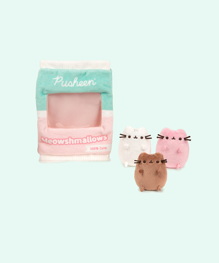 Front view of the miniature brown, white, and pink plush sitting outside of the Meowshmallows bag. The center portion of the bag is see-through.  