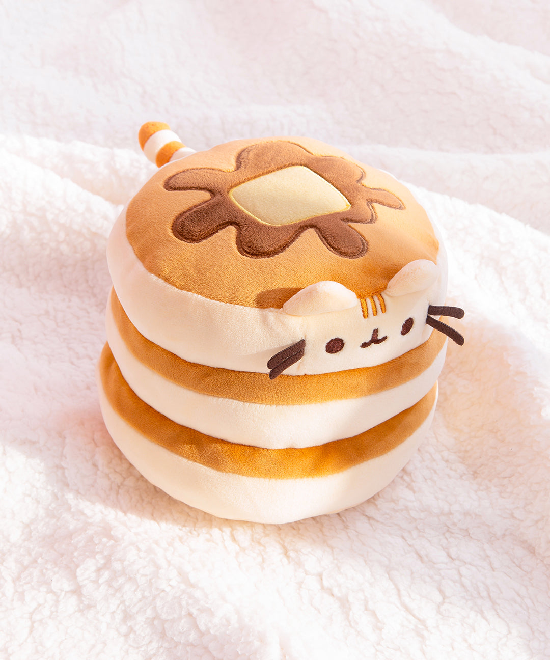 Top quarter view of pancake squisheen plush. Pusheen’s light brown and cream striped tail extends from the back of the stacked plush.