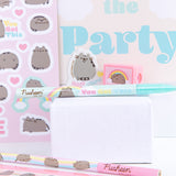 Close-up view of the contents of the Pusheen stationery set. The ruler, pencil, pen, sticker sheet, eraser, pencil sharpener, and notebook include graphics of a grey and brown Pusheen with yellow, pink, blue, and light teal details.  