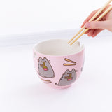 A hand holding the chopsticks over the Pusheen Ramen Bowl from the right, in front of a white background. 