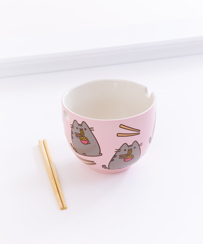 The Pusheen Ramen Bowl with the pair of chopsticks resting on the ground to the left, in front of a white background.