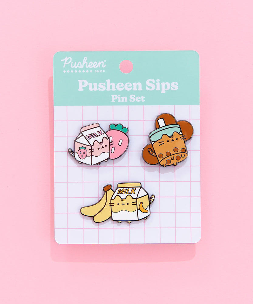Pusheen Sips Pins are attached to a cardboard backing featuring a grid interior. The pin set is lying on a pink backdrop. 