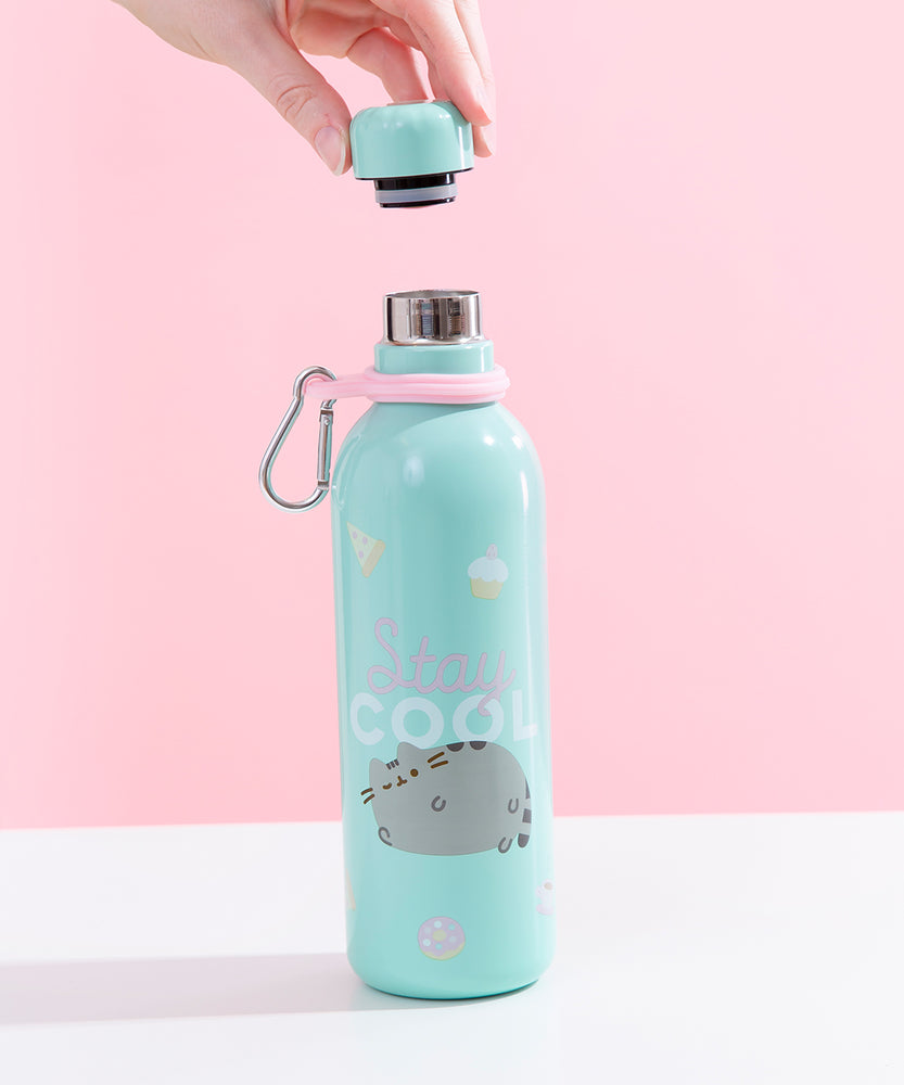 The Pusheen Stainless Steel Waterbottle with it’s cap removed, being held above the bottle by a model’s hand, in front of a white and pink background. The cap has a black stopper with a grey rubber seal, and the rim of the bottle is steel.