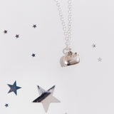 Close up of the silver Pusheen charm necklace, surrounded by reflective silver stars of various size. The details of Pusheen’s face are carved into the charm, while her ears and tail are molded as part of the charm. The loop connecting the charm to the chain necklace is on top of pusheen’s back.