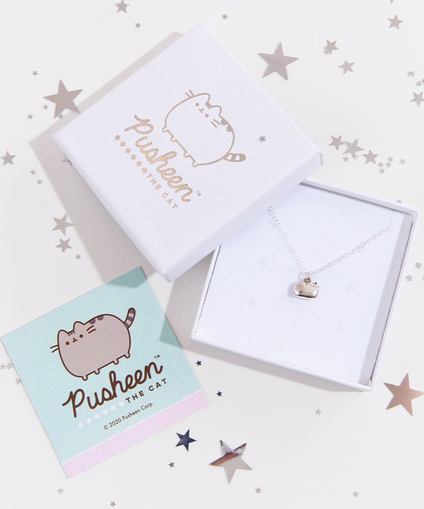 The silver charm necklace in a square white jewelry box, the box lid partially leaning on top of it, the square card insert laying underneath it, all surrounded by reflective stars of varying sizes.