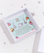 The back of the square card insert, featuring a photo of the silver Pusheen charm, alongside some copy regarding other charms from the manufacturer licensed to charm. Illustrations of various foods decorate the edges of the card.