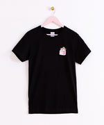 Front view of the Strawberry Milk Sips Tee. The black T-shirt is hanging on a light pink hanger in front of a white background. 