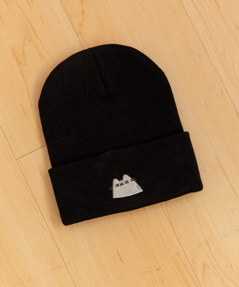 Top view of black knit hat laid on a light yellow hardwood surface.