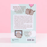 The back of the Pusheen the Cat book resting on top of a white desk. The back cover features copy, illustrations of Pusheen floating with a balloon and Pusheen in front of a computer. The barcode and publisher information is listed at the bottom of the book.
