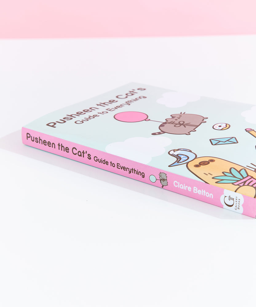 The Pusheen book lying on top of white surface to show off the pink book spine with Pusheen floating using a balloon.