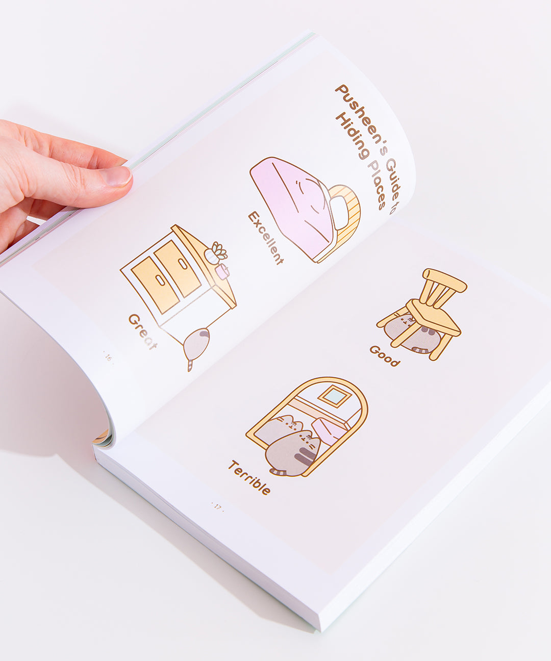 A model holding the book open in front of a white background, showing off the pages featuring a two-page comic of "Pusheen's Guide to Hiding Places."