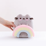 Model’s hand loosely holding the Pusheen with Rainbow Plush in front of a white background.