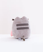 Back view of the Pushen with Rainbow Plush in front of a white background. Pusheen’s back has the standard two back stripes and a striped tail. Pusheen’s whiskers and rainbow stick out partially from the other side. The information tag for the plush is located to the left of the tail.