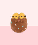 Front view of Chocolate Dipped Cookie Squisheen. Pusheen the Cat is shown in yellow with her classic eyes, mouth, and whiskers. The bottom portion of the plush is brown and has rainbow assortment of blue, green, white, and pink embroidered lines to look like sprinkles. 