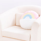 The Rainbow Pusheen Plush Pillow resting in a cream arm chair in front of a white background, turned around to show the back. The back of the pillow mirrors the rainbow and the cloud, but Pusheen is absent. The rainbow ends with a patch of white fabric, and the cloud goes straight through the middle of the pillow.