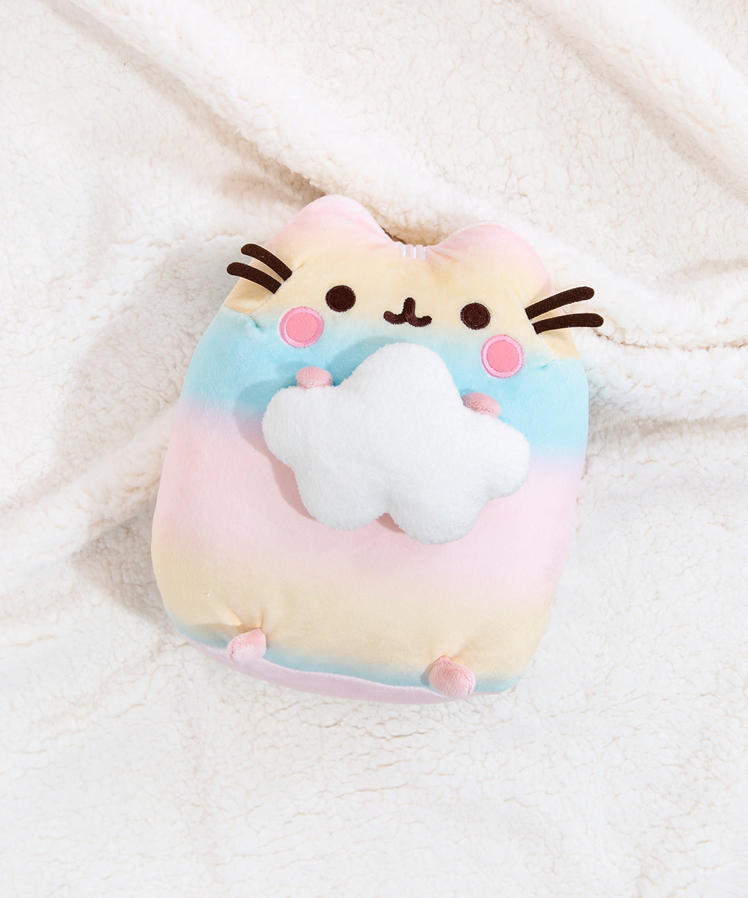 Top view of the Rainbow Pusheen Plush laying down on top of a fuzzy white blanket.