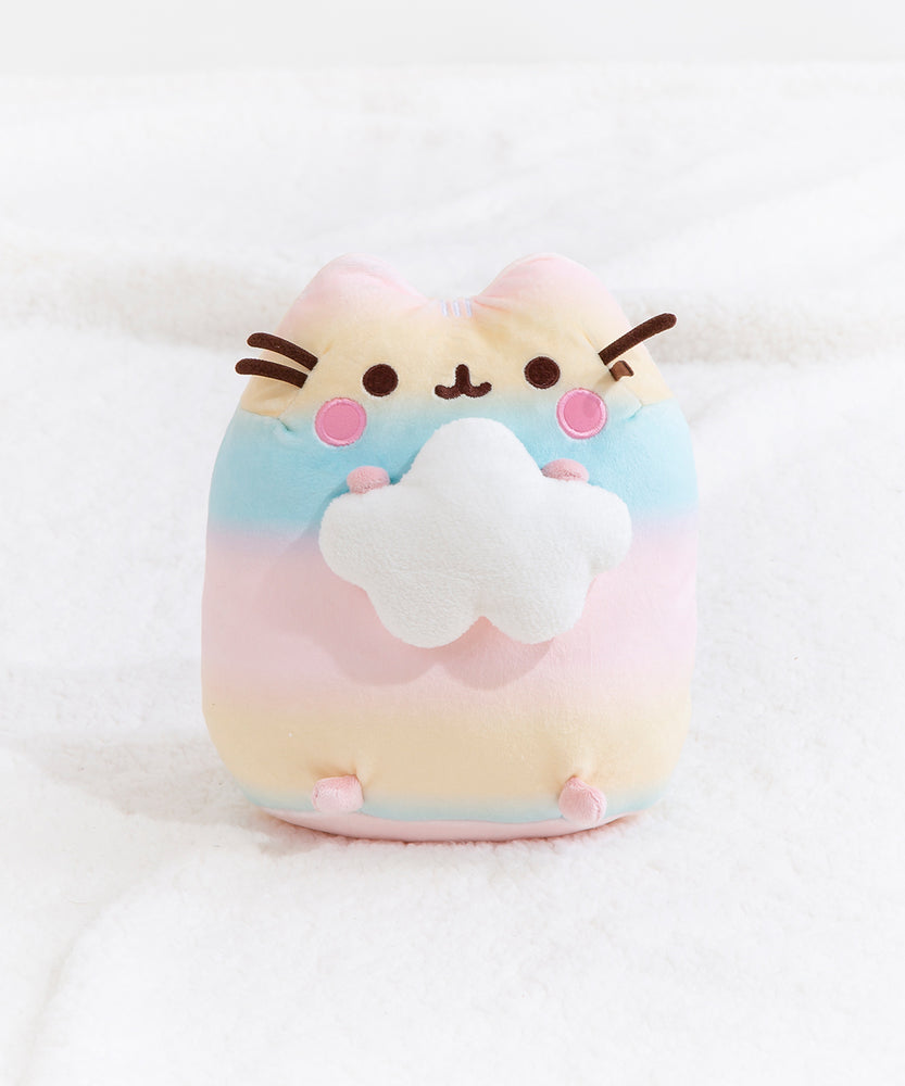 The Rainbow Pusheen Plush sitting upright in a fuzzy white space, matching the cloud Pusheen is holding.