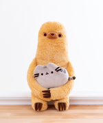 Front view of the Sloth plush holding the mini Pusheen plush in his arms, sitting on a white ledge in front of a white wall. The mini Pusheen plush is about the same width as Sloth’s body. 