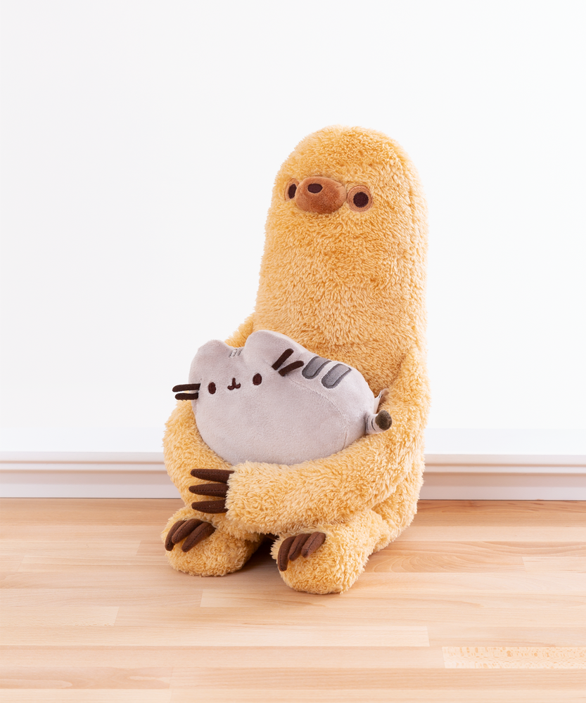 A quarter profile view of the Pusheen and Sloth Set facing the left, sitting directly on the wooden floor in front of a white background. It’s clear from this angle that Sloth sits directly on his base, and his legs point straight out. 