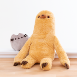 The Sloth plush sitting on the floor, arms uncrossed, with the mini Pusheen plush peeking out from behind him. Sloth’s arms start at the halfway point of Sloth’s body, and reach to the floor. There is a small square Velcro strip on the center of Sloth’s chest and on the palm of his hands that blend in with the color of his fur. Sloth’s legs are like cylinders, with the 3 brown plush claws placed on top of the foot. 