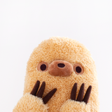 Close up of Sloth’s face peeking up from the bottom, hands to his face. Sloth’s snout is a darker brown and a smoother fabric then the rest of his fur. His nose is embroidered in dark brown directly on his snout. His snout is placed directly in between his eyes, which are dark brown embroidered dots with a light brown embroidered circle around them. Sloth’s claws are plush made with a felt-like fabric