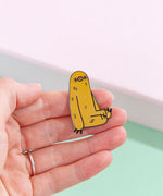 Model’s hand holding the sloth pin in front of a mint and pink background. The pin is small, only slightly taller then the width of two fingers.
