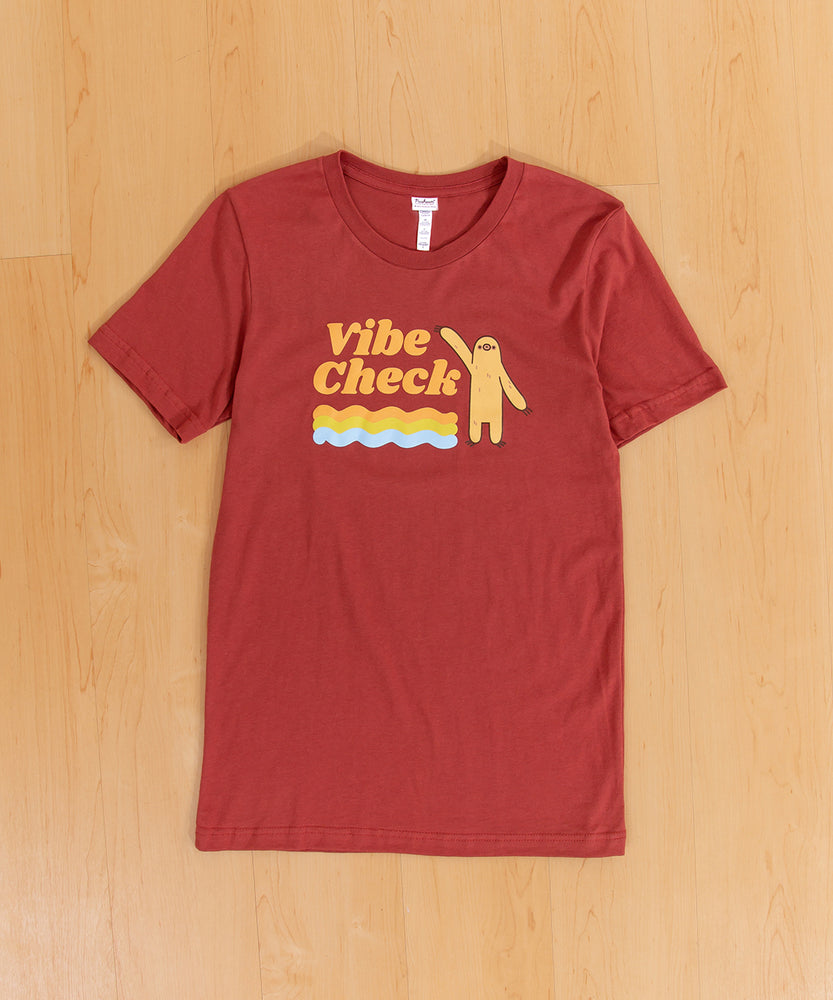 The Vibe Check tee laid out on a wooden floor 