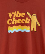 The Vibe Check tee laid out on a wooden floor 