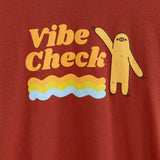 Close up of the screen printed graphic on the tee. The words ‘Vibe Check’ are in orange, and the squiggly lines end around bottom of Sloth’s feet.