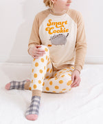 A model wearing the Smart Cookie Pajama Set sitting on top of a fuzzy white blanket. The top has a looser fit, while the pants fit more like leggings. 