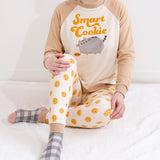 A model wearing the Smart Cookie Pajama Set sitting on top of a fuzzy white blanket. The top has a looser fit, while the pants fit more like leggings. 