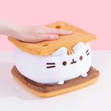Gif of Pusheen S'mores Squisheen being smooshed by model hand. Pusheen the Cat takes the form of a s'mores treat. The top and bottom slabs of graham cracker-inspired plush is a soft textured light brown fabric.
