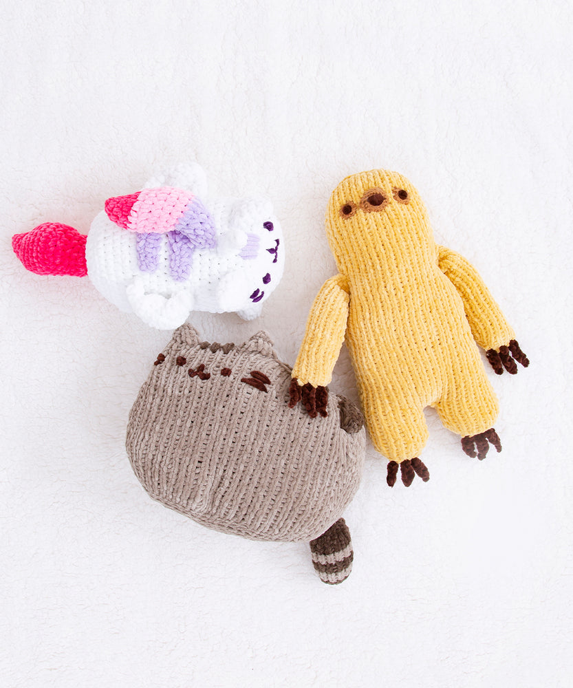 The Super Pusheenicorn, Pusheen, and Sloth crocheted plush laying on a fluffy white blanket