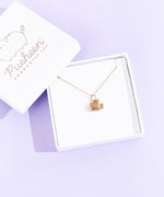 A small white square jewelry box with the lid removed and placed on the top left corner of the box holding the Gold Super Pusheenicorn Charm Necklace. The jewelry lid features the Pusheen the Cat logo printed in silver.