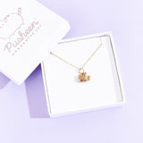 A small white square jewelry box with the lid removed and placed on the top left corner of the box holding the Gold Super Pusheenicorn Charm Necklace. The jewelry lid features the Pusheen the Cat logo printed in silver.
