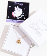 A small white square jewelry box with the lid removed and placed on the top right corner of the box holding the Gold Super Pusheenicorn Charm Necklace. Above is a black and light purple square card insert featuring an illustration of Super Pusheenicorn.