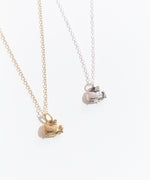 Two Super Pusheenicorn Charm Necklaces, one gold and one silver, lay next to each other on top of a white background.