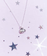 Top view of the Silver Super Pusheenicorn Charm Necklace on top of a light purple background, surrounded by reflective silver stars.