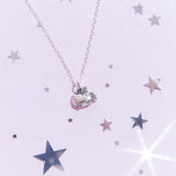 Top view of the Silver Super Pusheenicorn Charm Necklace on top of a light purple background, surrounded by reflective silver stars.