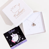 A small white square jewelry box with the lid removed and placed on the top left corner of the box holding the Silver Super Pusheenicorn Charm Necklace. To the left is a black and light purple square card insert featuring an illustration of Super Pusheenicorn.