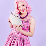 Front view of smiling model wearing Super Pusheenicorn Dreamer Dress while holding a medium-size plush of Pusheen the Cat in their hands.  