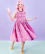 Model walking in the pink Super Pusheenicorn Dreamer Dress while holding a strawberry milkshake. The dress hem is swaying and reveals the repeating pattern of Super Pusheenicorn and celestial objects.  