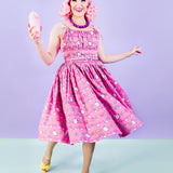Model walking in the pink Super Pusheenicorn Dreamer Dress while holding a strawberry milkshake. The dress hem is swaying and reveals the repeating pattern of Super Pusheenicorn and celestial objects.  