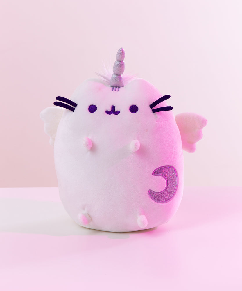 The Super Pusheencorn plush in front of a white background, bathed in a magenta light. The Super Pusheenicorn plush reflects the light around her and appears light pink as a result.
